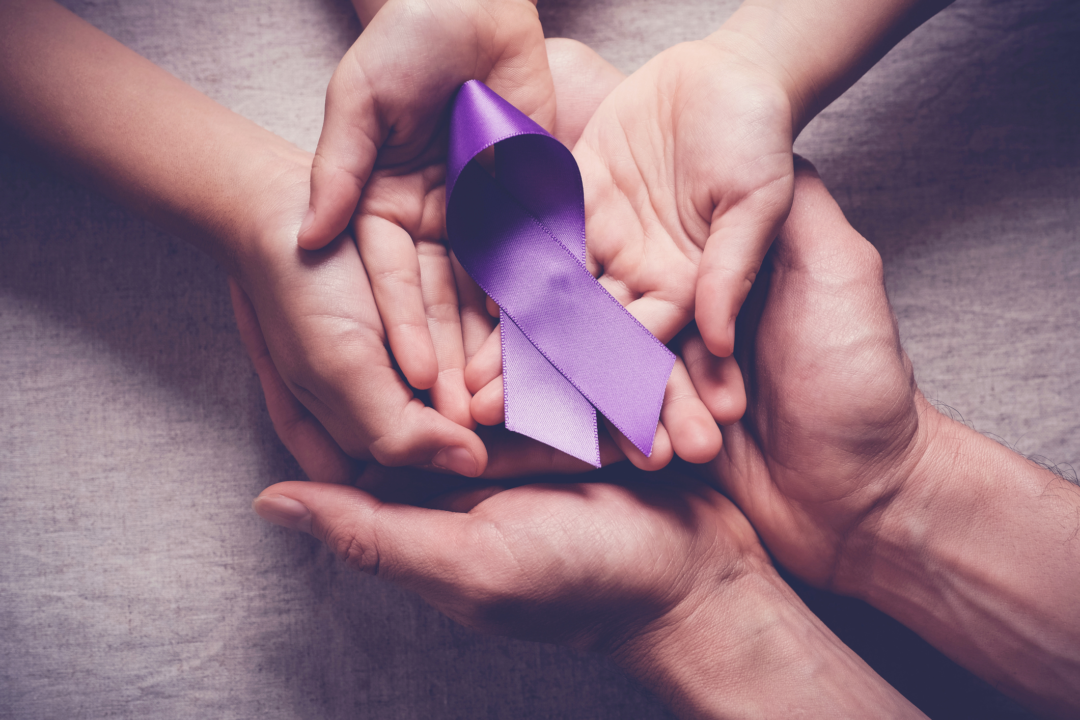 Hands holding a purple awareness ribbon.