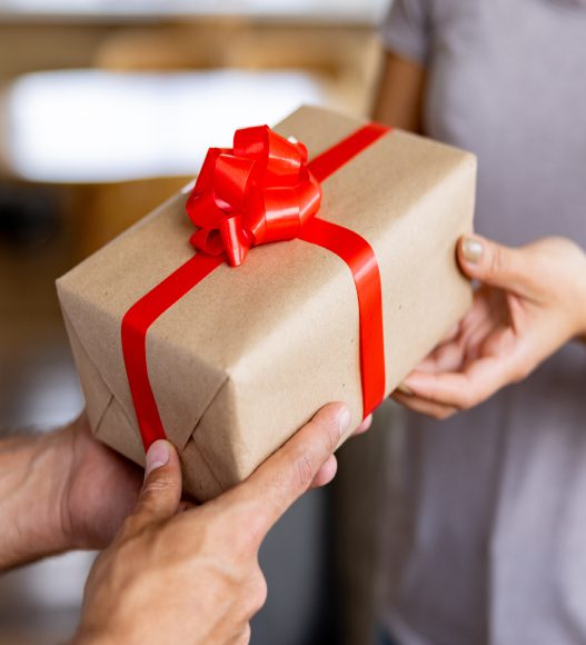 Hands exchanging a gift with red ribbon.